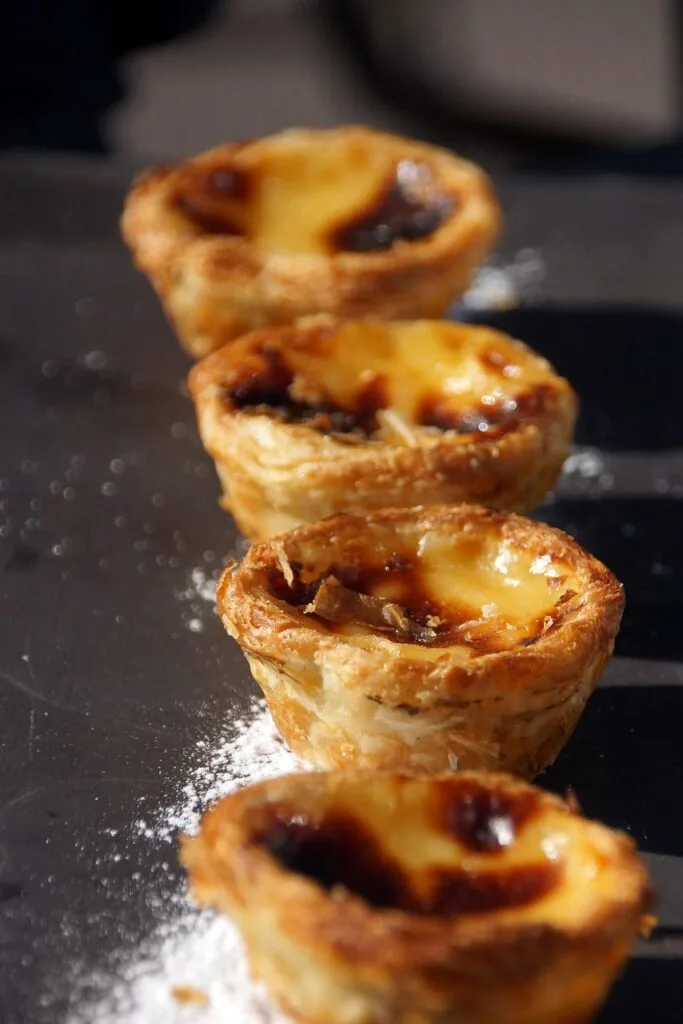 Gros plan sur une rangée de pastéis de nata dorés, bord croustillant