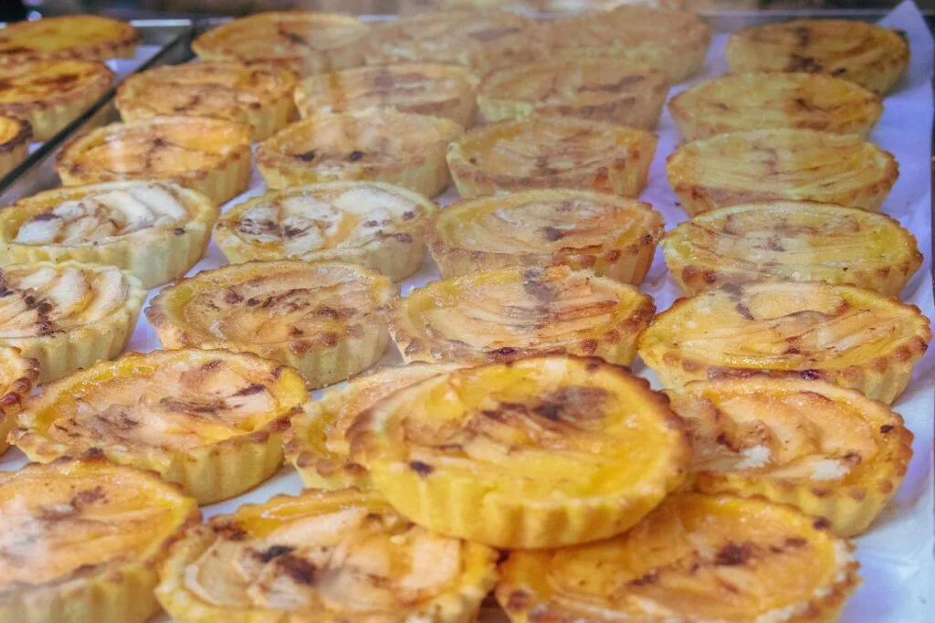 Tartelette feuilletée aux pommes alignées dans une vitrine de pâtisserie lisboète
