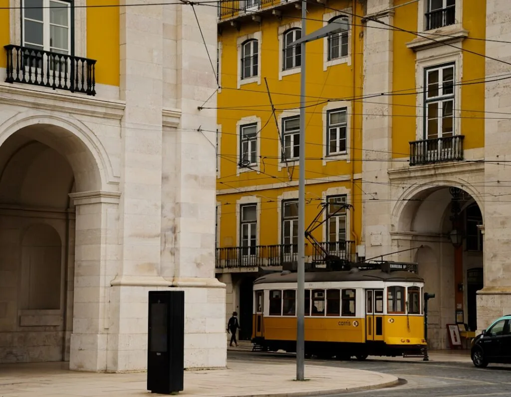 Tramway jaune historique circulant devant immeubles jaunes sous des arcs à Lisbonne
