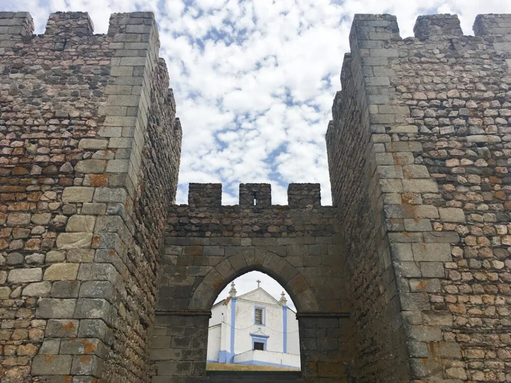 Arc de muraille en pierre encadrant une petite chapelle blanche et bleue.