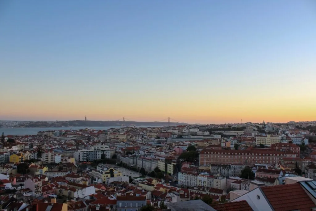 Panorama de Lisbonne au coucher, pont et rives lointaines visibles.