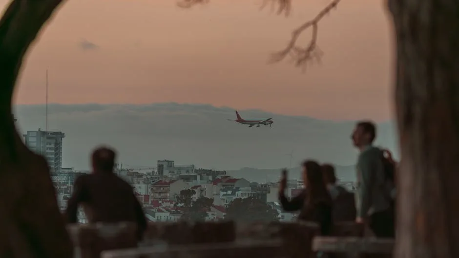 Avion en approche au-dessus de Lisbonne, silhouettes de visiteurs au belvédère.