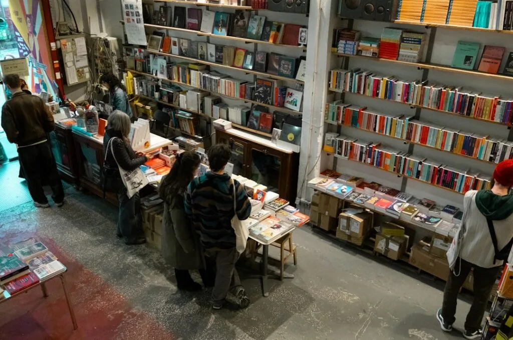 Librairie indépendante animée avec étagères hautes et clients feuilletant des livres.
