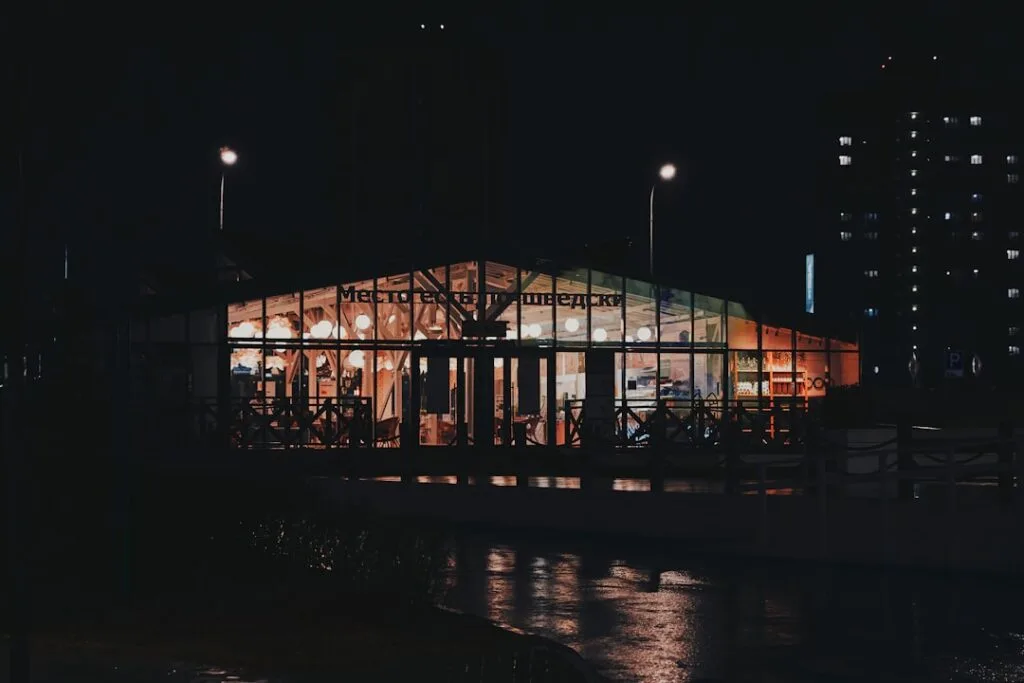 Kiosque vitré éclairé la nuit à Lisbonne, lumières chaudes et reflets mouillés