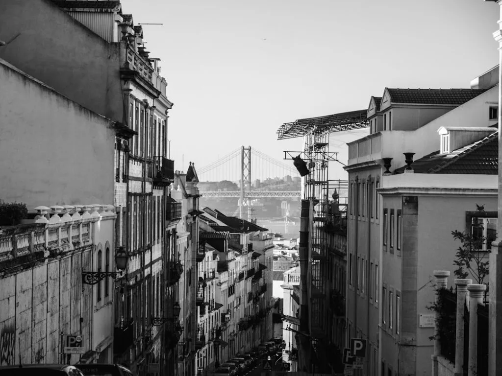 Vue en noir et blanc d'une rue pentue à Lisbonne, pont au loin